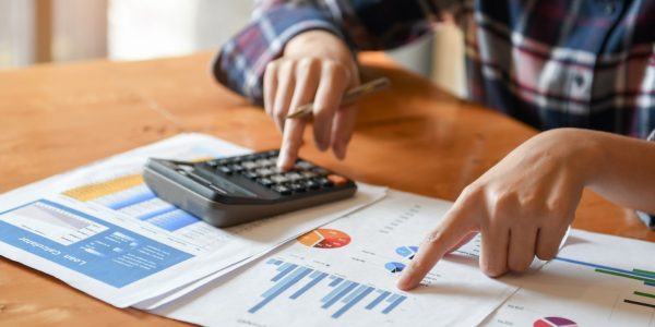 Hand pointer at graph and other hand hold pen and presses the calculator.