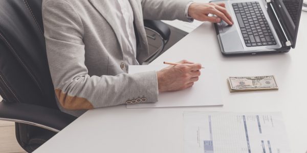 A male accountant works at a pc in an office at home. Payroll and cash withdrawal